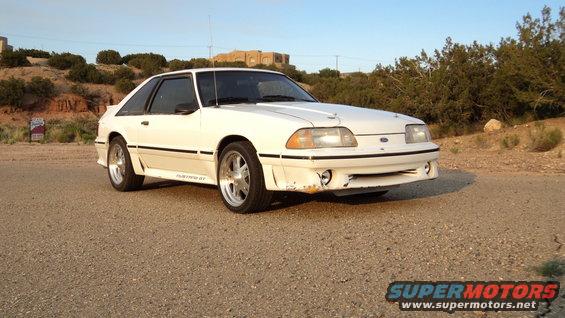 White 1989 Ford Mustang GT parked on a dirt road with arid landscape in the background