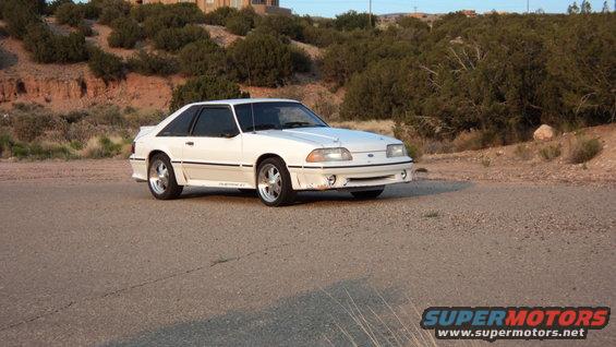 White 1989 Ford Mustang GT parked on a dirt road with hills and brush in the background