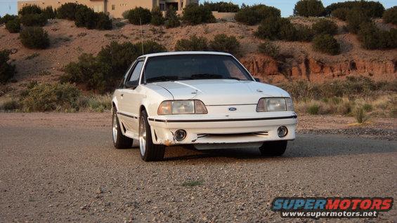 White Ford Mustang with front damage, parked on a gravel road