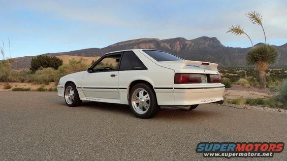 White 1987 Ford Mustang GT coupe parked on asphalt with desert mountains in background