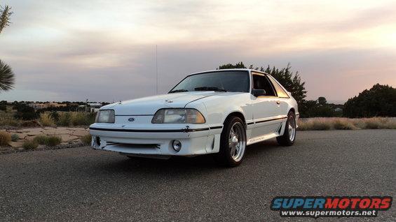 White 1989 Ford Mustang coupe with body kit parked on asphalt