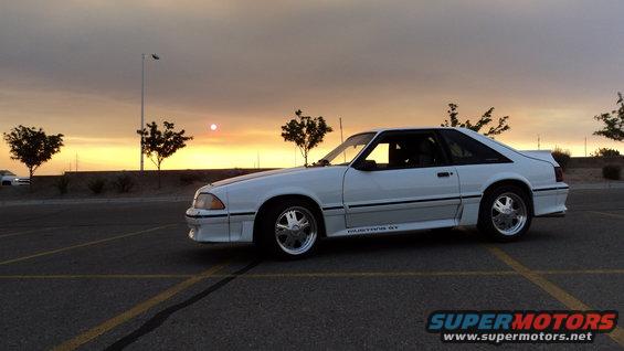 White Ford Mustang GT parked in a lot at sunset, side profile visible