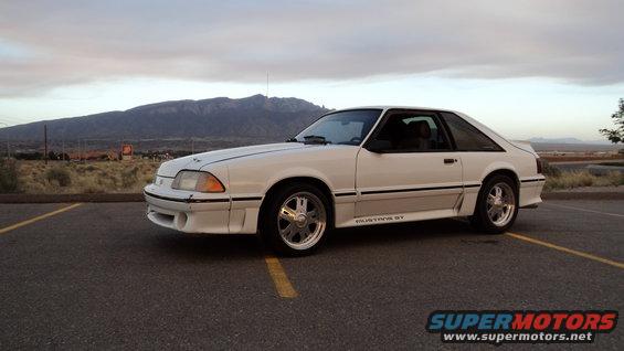 White 1987 Ford Mustang GT parked on asphalt with mountains in background