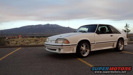 White 1989 Ford Mustang GT coupe parked in a lot with mountains in the background