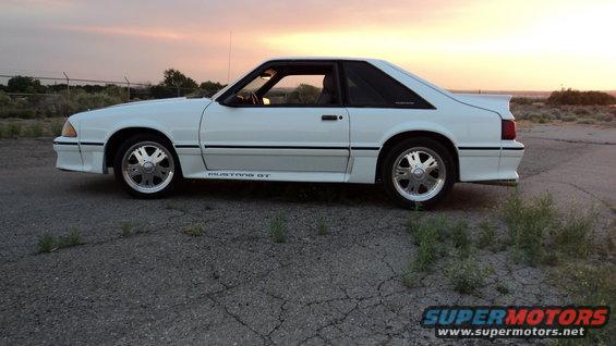 White 1989 Ford Mustang GT parked on gravel lot at sunset