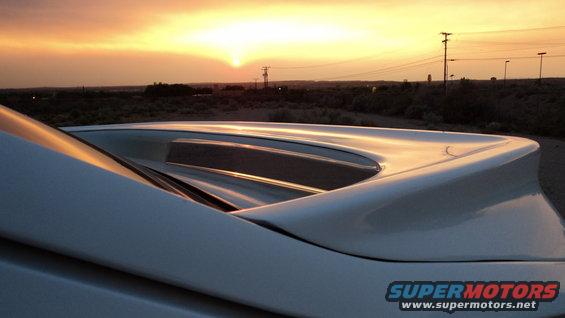 White car's rear spoiler against a sunset sky with utility poles in the distance