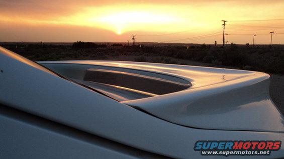 Close-up of a white car's rear spoiler with a sunset in the background
