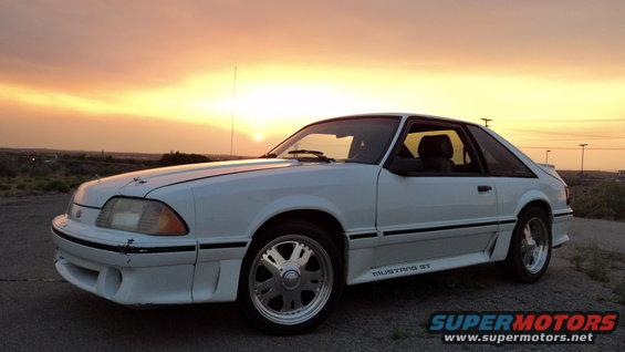 White 1987 Ford Mustang GT coupe with aftermarket wheels parked outdoors at sunset
