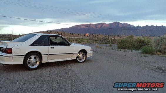 White 1989 Ford Mustang GT coupe parked roadside with mountains in background