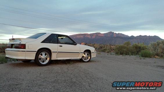 1989 Ford Mustang coupe parked on a dirt road with mountains in the background