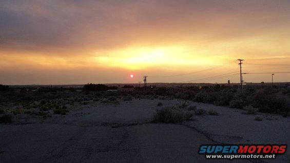 Sunset with orange and yellow sky over a desert landscape with power lines and a distant town