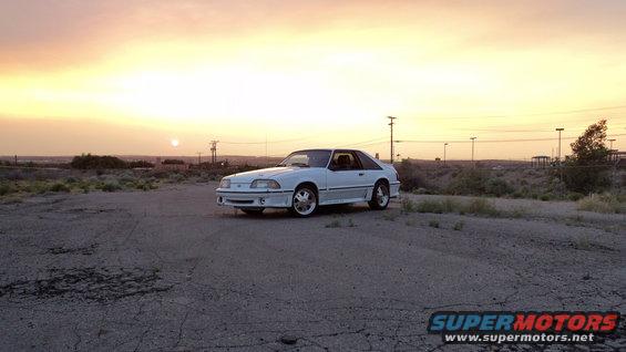 White coupe car parked on dirt lot with sunset in background