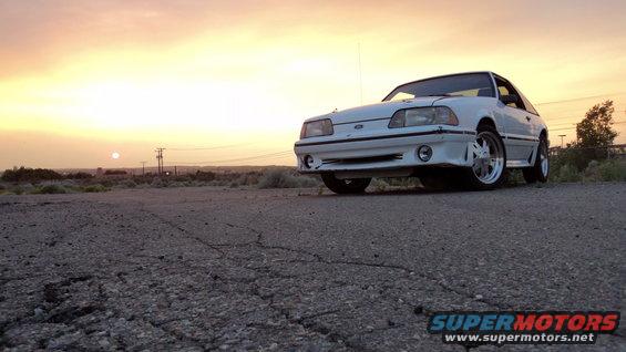 White 1989 Ford Mustang coupe parked on cracked asphalt at sunset