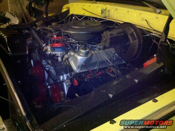 Yellow vehicle engine bay with V8 engine, distributor, and air cleaner. Visible red fan shroud