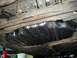 1989 Ford Probe - The undercarriage of a vehicle shows a large black fuel tank and rusted suspension parts.
