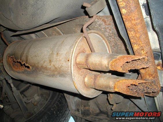 Dual exhaust pipes on a rusty muffler, viewed from below