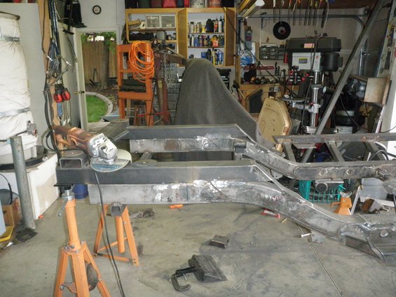 Modified vehicle frame on jack stands with an angle grinder nearby in a garage