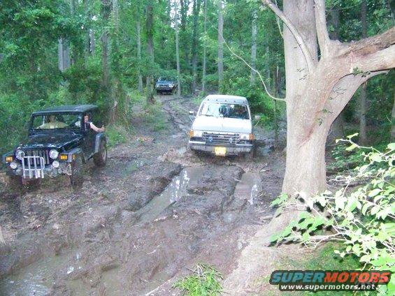 Jeep Wrangler and van driving through mud in a forest, with another vehicle behind
