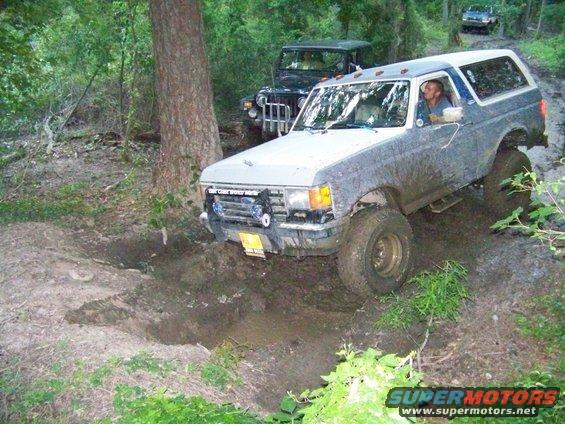 Ford Bronco navigating a muddy trail with a Jeep behind it