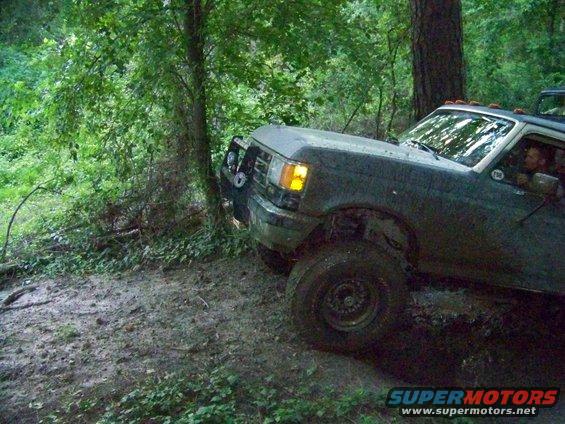 Dark green Ford F-Series truck with off-road tires driving through mud and trees