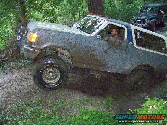 Mud-covered SUV with lifted suspension driving through mud, another Jeep in background