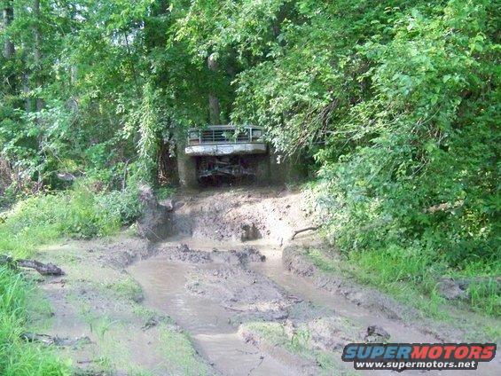 White Ford Bronco driving through mud, front view. Grille and headlights visible