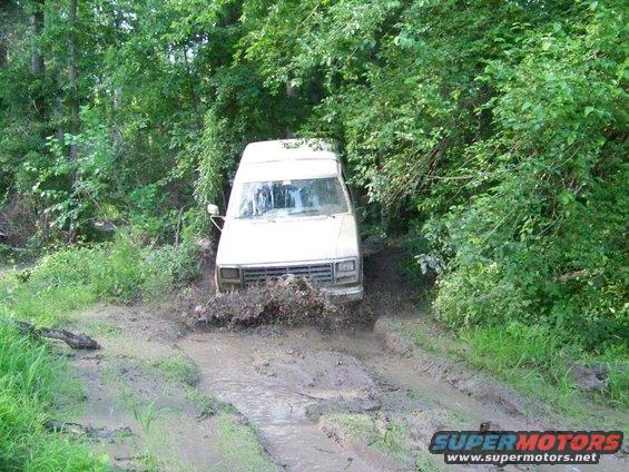 White van splashing through mud on a wooded trail