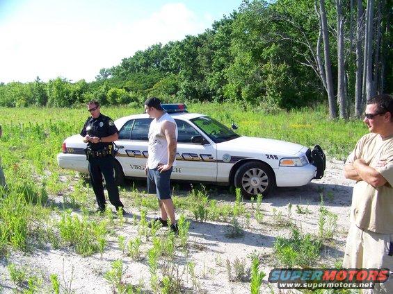 Virginia Beach police car parked in a grassy field with two men standing nearby