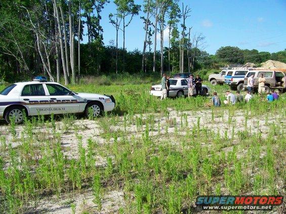 police cars and several off-road vehicles parked in a grassy field with people standing around