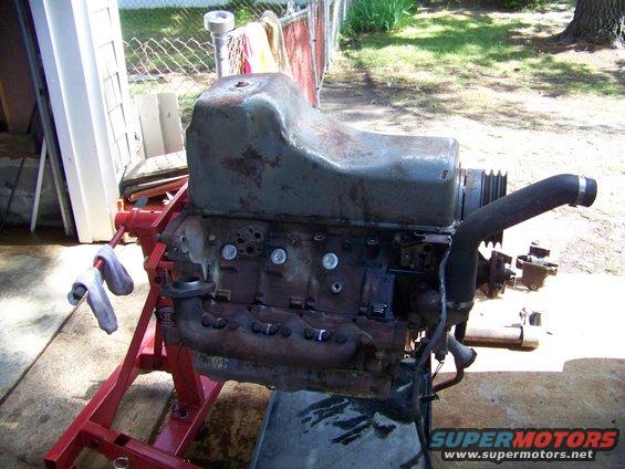 Engine on a red stand, viewed from the side, with exhaust manifold and intake pipe visible