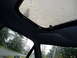1993 Ford Bronco - Rain streaks down the sunroof and side window, obscuring the view of the trees and houses outside.