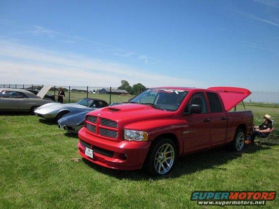 Red Dodge Ram pickup truck with hood scoop and open tonneau cover parked on grass