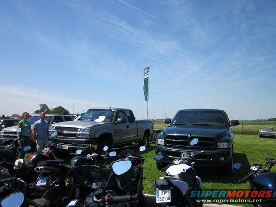 Two pickup trucks and motorcycles parked on grass under a blue sky