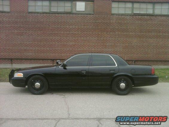 Black 2004 Ford Crown Victoria sedan, side view, parked on asphalt in front of a brick building