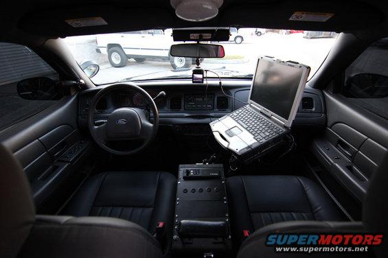 2004 Ford Crown Victoria interior showing dashboard, steering wheel, laptop mounted on console, and black leather seats
