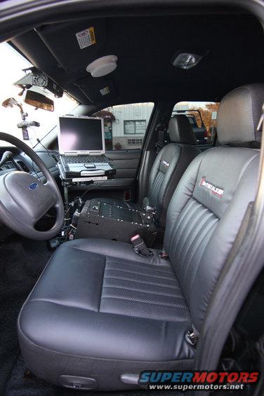 Interior of a police car showing front seats, laptop, and console
