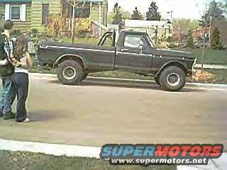 Black Ford F-Series pickup truck, lifted with large tires. Two people stand nearby