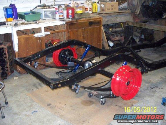 Vehicle frame on dollies with red wheels and blue shocks. Engine block visible to the left