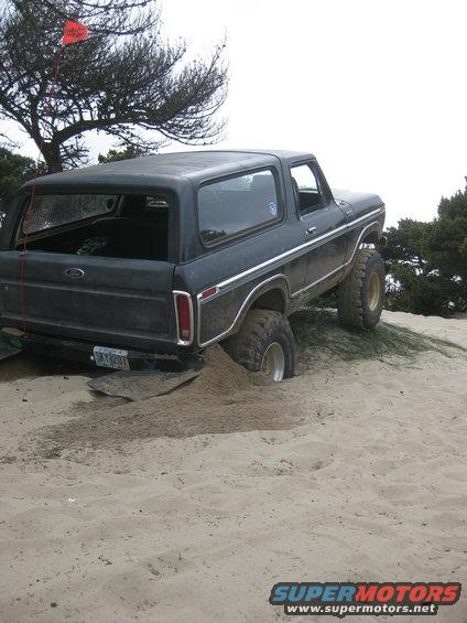 Black 1979 Ford Bronco stuck in sand dune with rear wheel buried