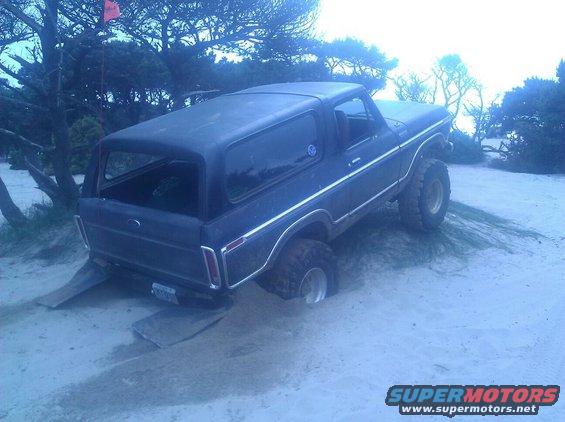 Dark blue Ford Bronco with lifted suspension stuck in sand, rear wheels on ramps