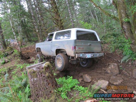 GMC K5 Blazer driving on a dirt trail in the woods, going over rocks
