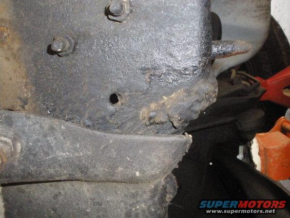 Close-up of a rusty, black metal vehicle frame section with bolts and a hole