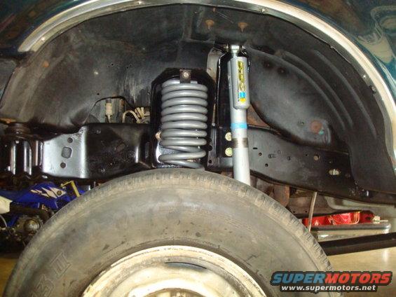 Close-up of a vehicle's front suspension with a coil spring and Bilstein shock absorber, partially obscuring a tire