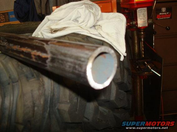 Metal pipe resting on a large tire, with a drill press in the background