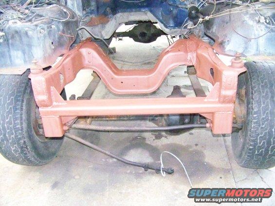 Vehicle frame with red-painted suspension components and front wheels. Some wiring is visible