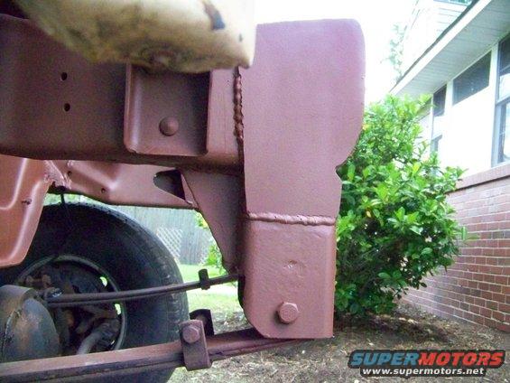 Close-up of a painted metal bracket attached to a vehicle frame, with leaf springs and a tire visible