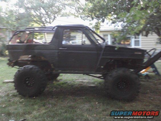 Black modified Ford Bronco with large tires and roll cage, seen from the side