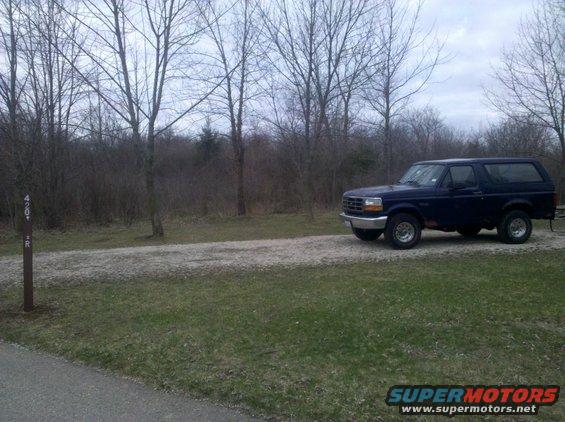 Dark blue 1995 Ford Bronco parked on gravel road with trees in background