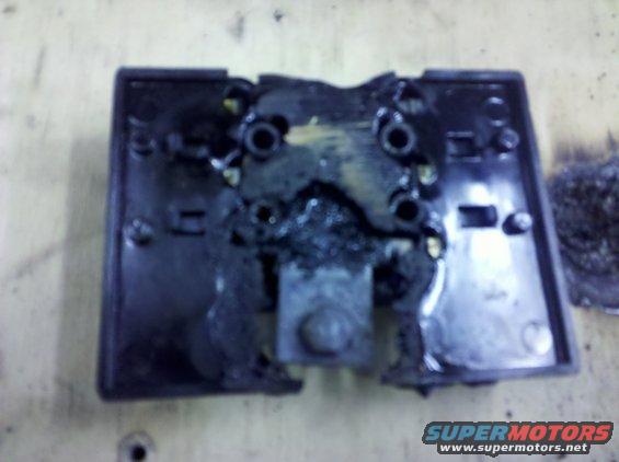 Damaged black plastic part with melted components and visible Supermotors.net logo