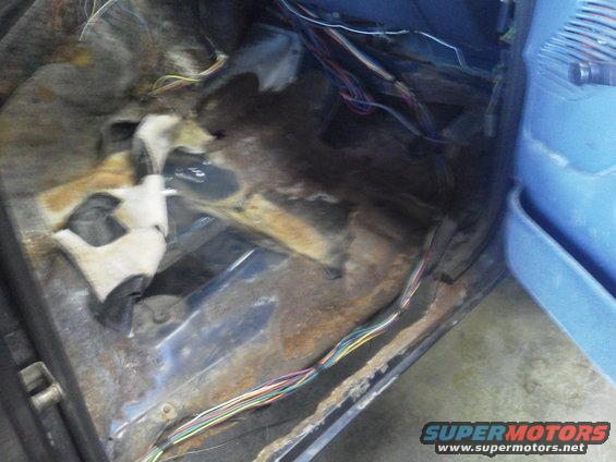 Interior floor of a vehicle showing significant rust and exposed wiring harness
